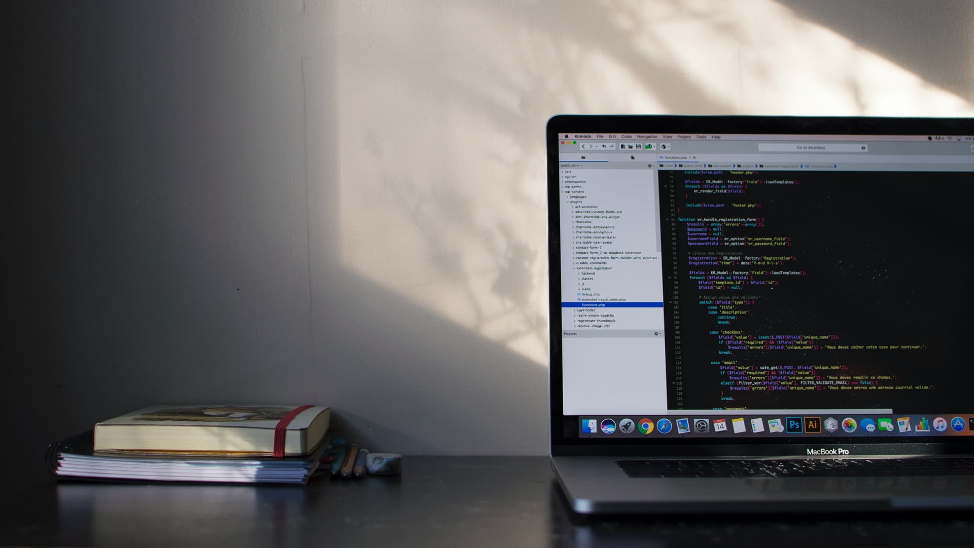 A laptop showing source code beside notebooks on a desk.